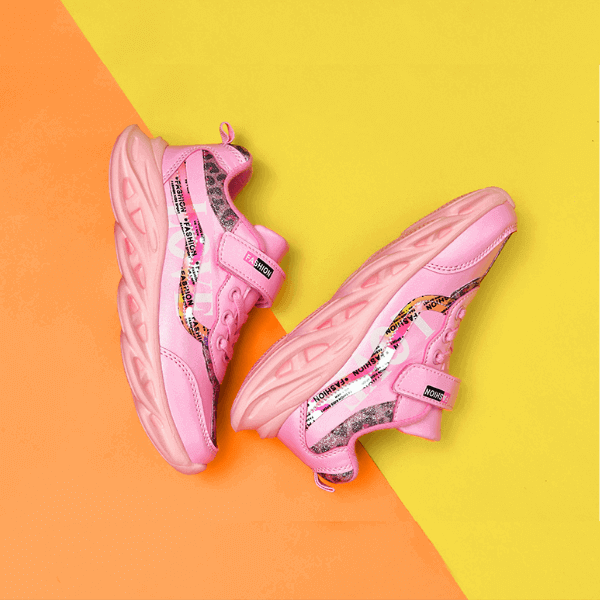 Girls pink sneakers with Velcro straps and patterned accents on a two-tone orange and yellow background