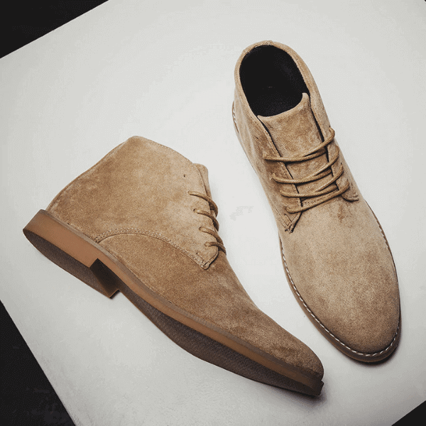 Pair of stylish men's suede boots in tan with laces and rubber soles on a white background
