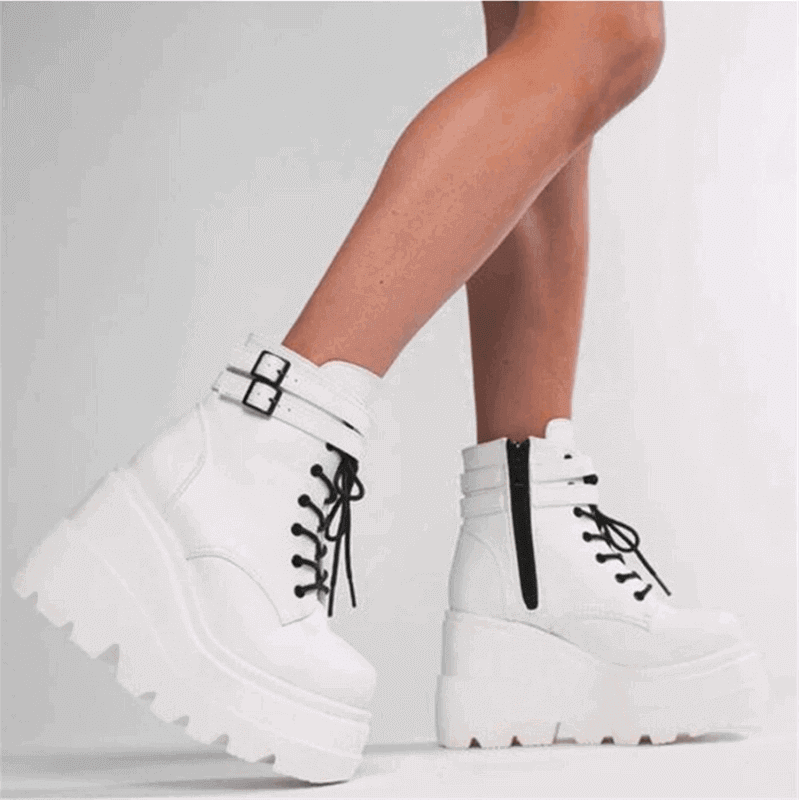 White women's platform boots with chunky soles, black laces, and buckle straps on model's legs